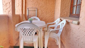 En lille terrasse med et bord, stole, en plantekasse og et vindue med træramme.