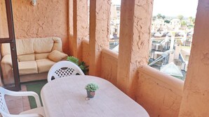 En balkon med et hvidt bord, en beige sofa og en potteplante.