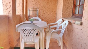 Un pequeño patio con una mesa, sillas, una planta en maceta y una ventana con marco de madera.