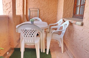 Une petite terrasse avec une table et des chaises, un pot de fleurs et une fenêtre avec un cadre en bois.