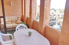 Un balcon avec une table blanche, un canapé beige et une plante en pot.