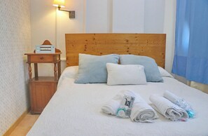 Un lit bien fait, avec des oreillers, une tête de lit en bois, une table de chevet avec une lampe et des serviettes enroulées posées sur le lit.