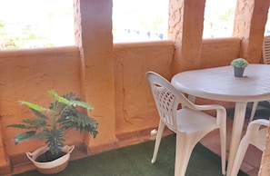 Un patio con una mesa redonda y dos sillas, una planta en maceta y vistas a través de una ventana.