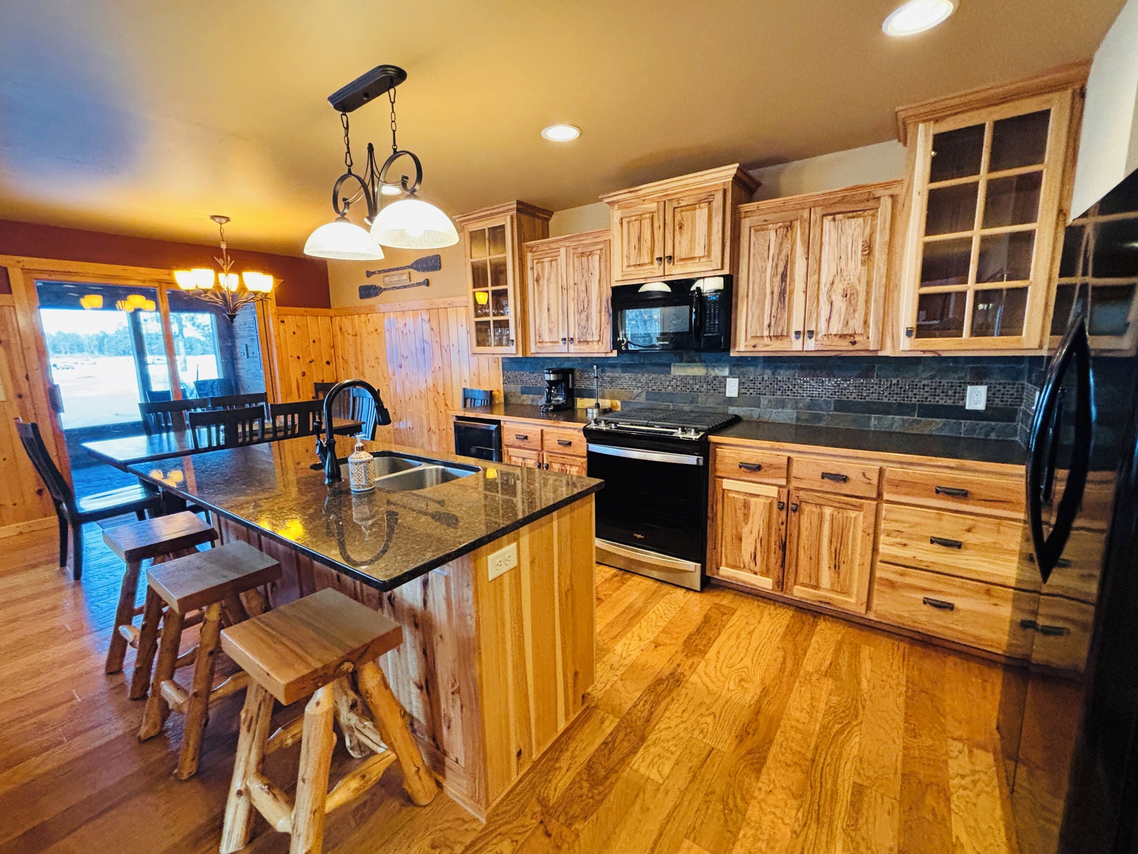 A kitchen with wooden cabinets, a central island with stools, a microwave, and a refrigerator.