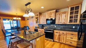 A kitchen with wooden cabinets, a central island with stools, a microwave, and a refrigerator. - Lakefront Luxe - Antler Cottage a 3-Level Retreat on the Whitefish Chain (Pequot Lakes)