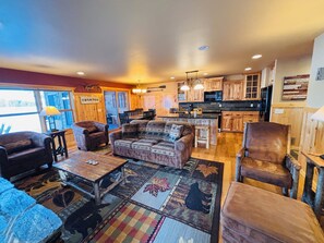 Ein geräumiges Wohnzimmer mit einer großen Eckcouch, einem Couchtisch und einem Kamin. Der Küchenbereich ist sichtbar, mit Holzschränken und einer Kochinsel.