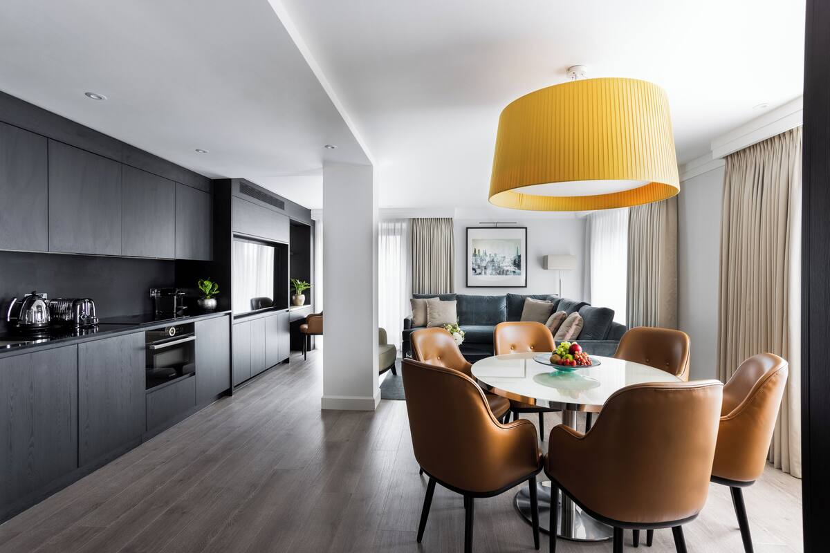 A modern kitchen with dark cabinets, a dining area with a round table and leather chairs, and a large yellow pendant light.