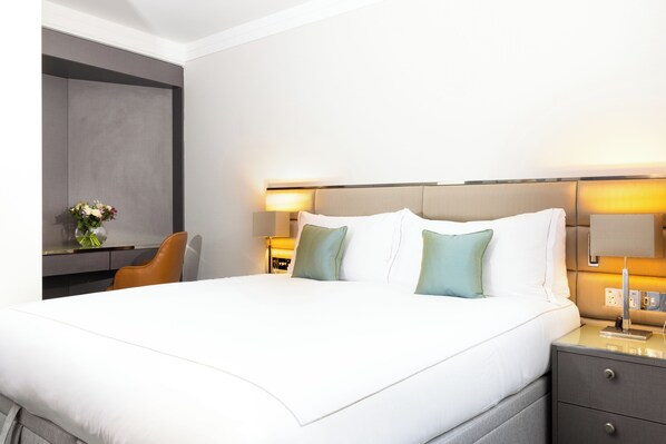 Une chambre d’hôtel avec un grand lit, deux lampes de chevet, un bureau avec une chaise et un vase de fleurs.