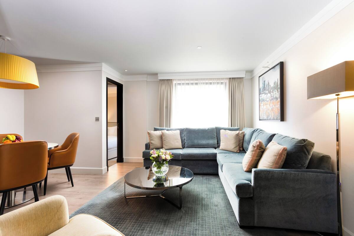 A modern living room with a grey sofa, a round coffee table, and a dining area with orange chairs.
