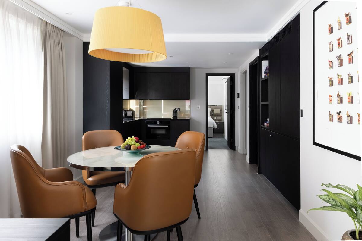 A modern dining area with a round table, four chairs, and a yellow pendant light.