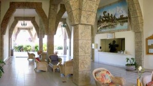 A lobby with stone columns, wicker furniture, a reception desk, and a mural. - Paradise to live in! (Nuevo Vallarta)