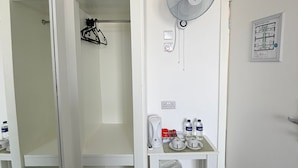 A hotel room with a walk-in closet, a standing fan, a small table with toiletries, and a wall-mounted thermostat. - The Gate Hotel (London)