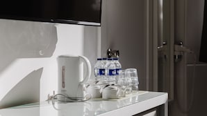 A hotel room with a flat-screen TV mounted on the wall, a white countertop with a coffee maker, water bottles, and glasses. - The Gate Hotel (London)