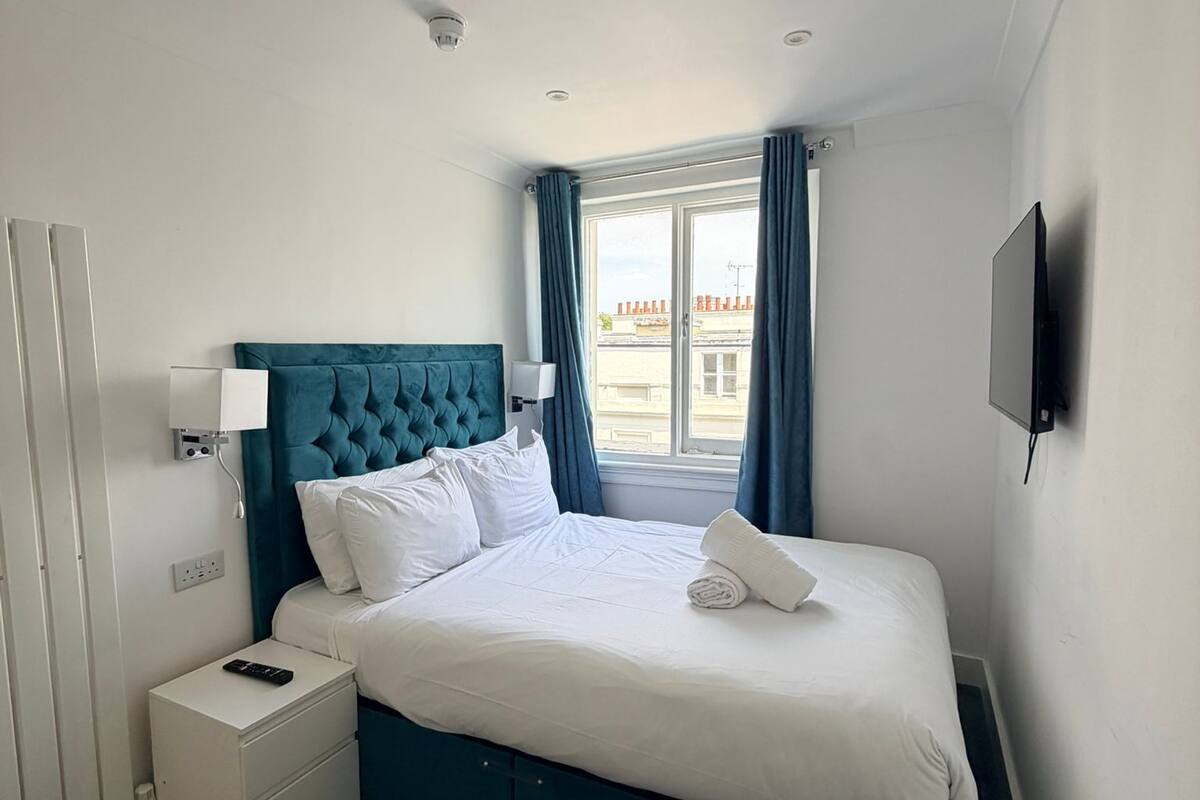 Une chambre d’hôtel avec un lit, une table de chevet, une télévision et une fenêtre avec des rideaux.