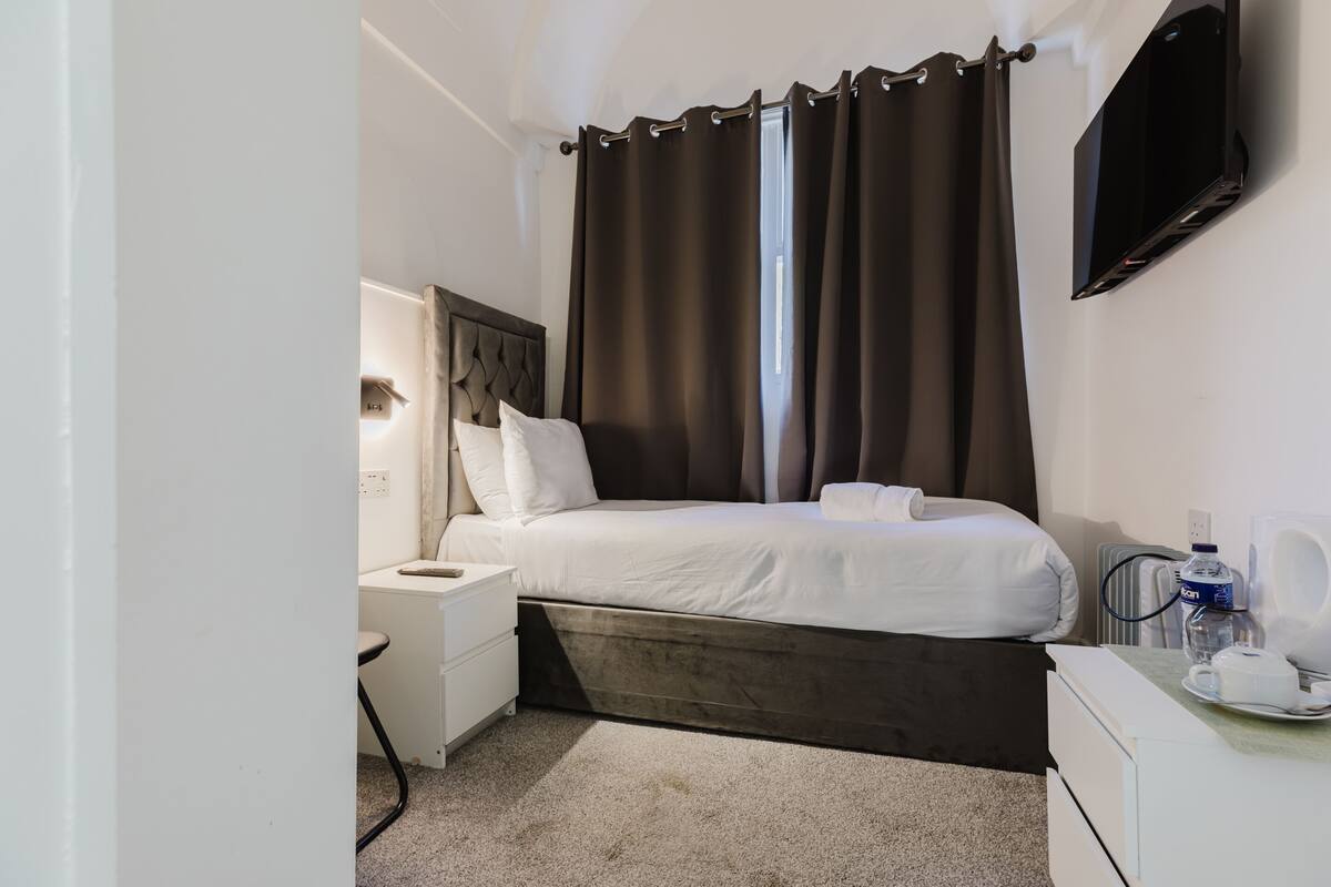 Une chambre d’hôtel équipée d’un lit, d’une table de chevet, d’une lampe et d’un téléviseur à écran plat fixé au mur.