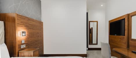 Una habitación de hotel con cama, mesita de noche de madera, televisor, escritorio y silla.