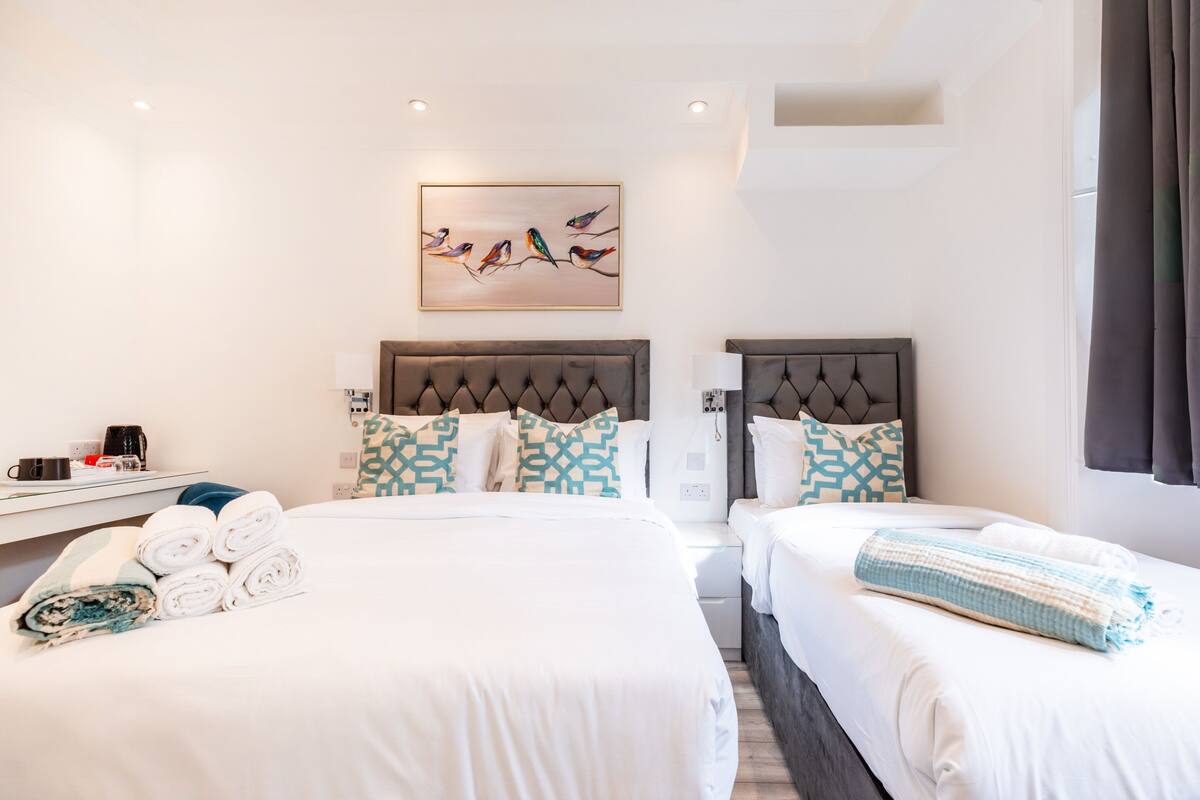 Une chambre d’hôtel avec deux lits, un tableau représentant des oiseaux accroché au mur et une fenêtre avec des rideaux.