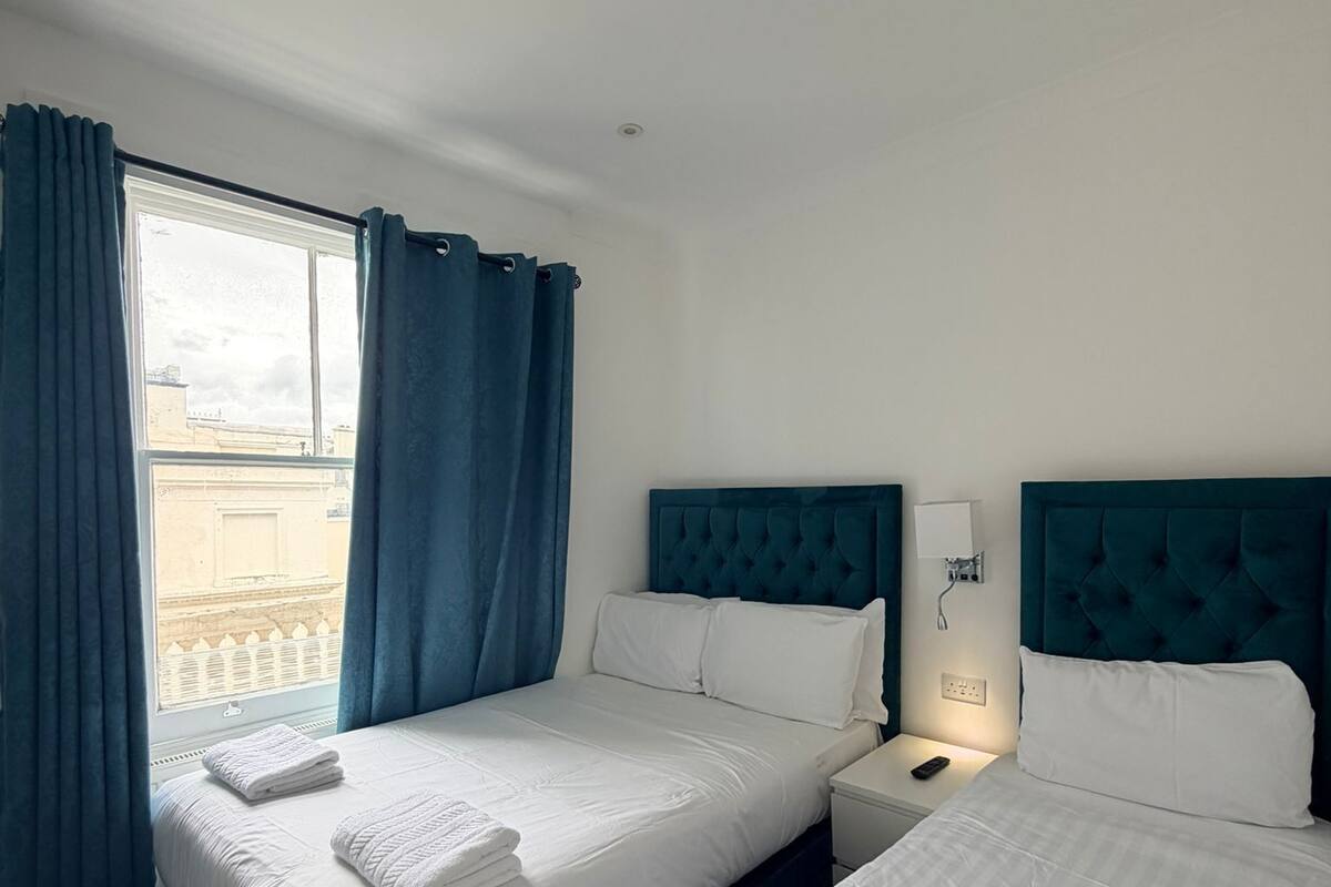 Une chambre d’hôtel avec deux lits, une fenêtre avec des rideaux et une vue sur les bâtiments environnants.