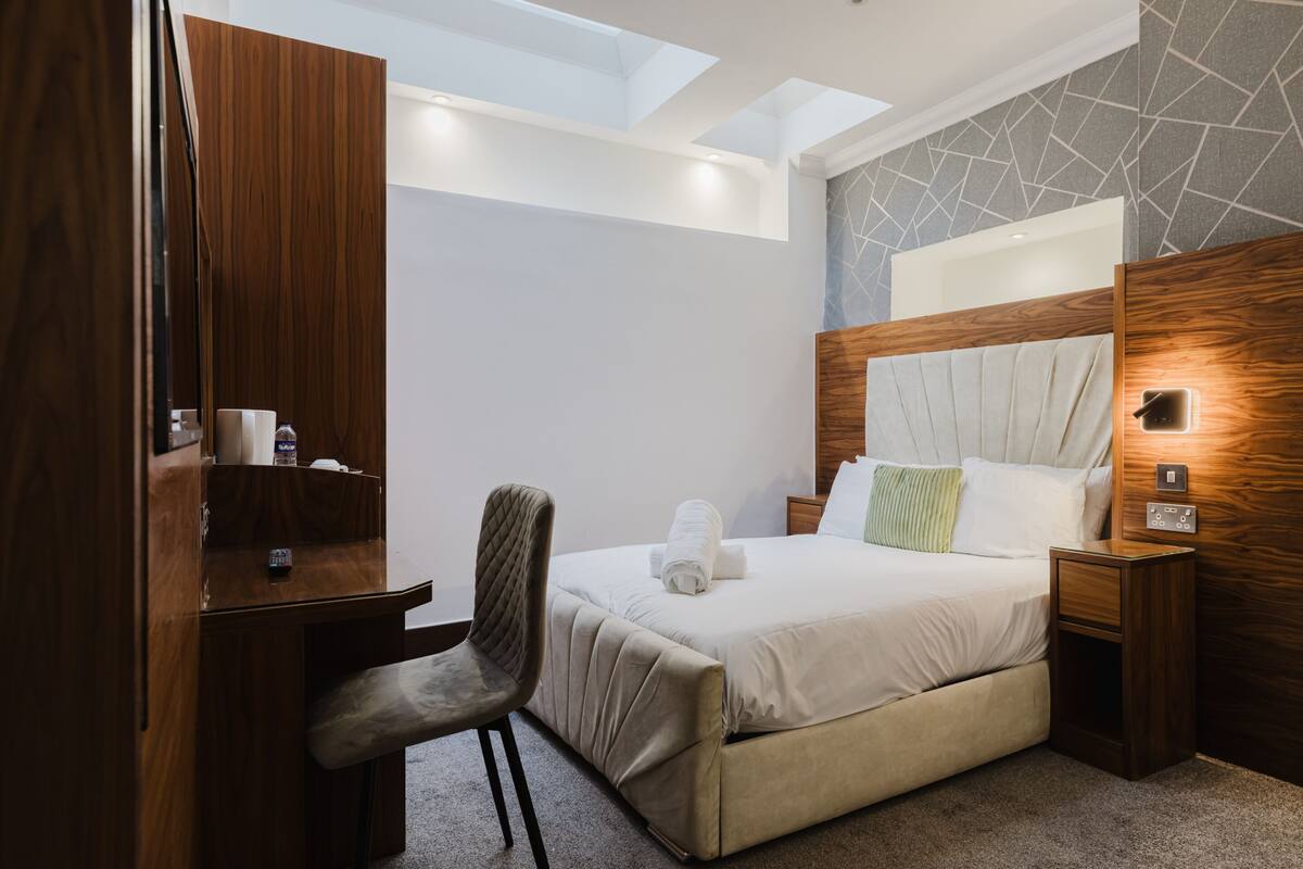 Une chambre d’hôtel moderne équipée d’un lit, d’un bureau, d’une chaise, d’une table de chevet et d’une fenêtre de toit.
