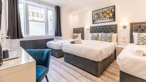 A hotel room with two beds, a desk, a chair, and a large window. - The Gate Hotel (London)
