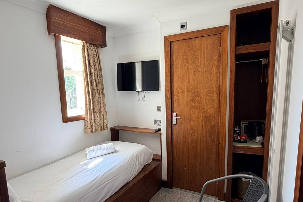 Une chambre à coucher de taille réduite, comprenant un lit, un téléviseur, une armoire en bois et une chaise.