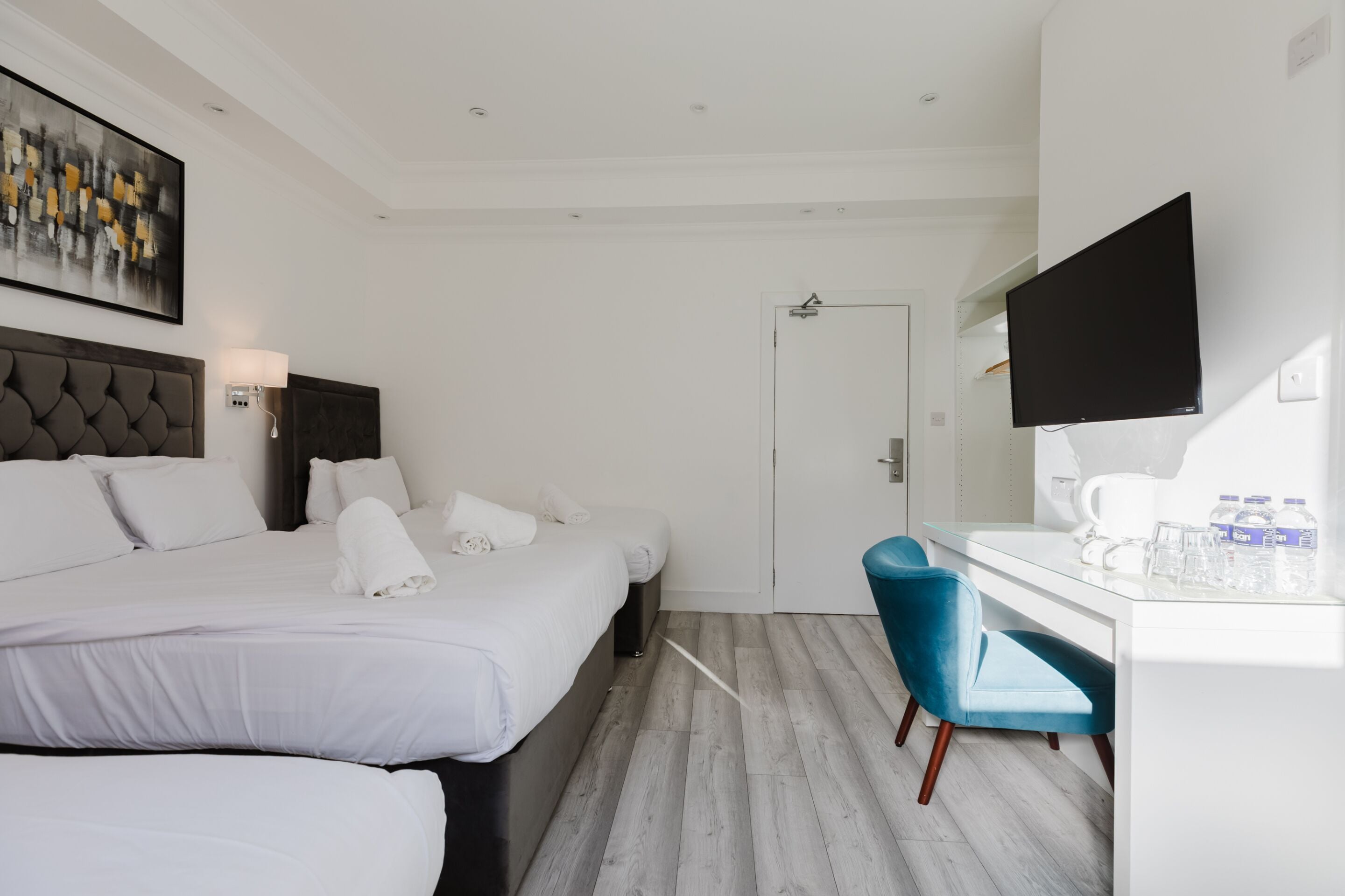 A hotel room with a bed, a desk, a chair, a flat-screen TV, and a painting on the wall.