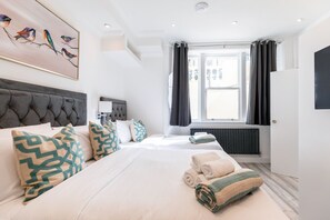A hotel room with a large bed, two bedside tables, a headboard, a window with curtains, a radiator, and a painting of birds on the wall. - The Gate Hotel (London)
