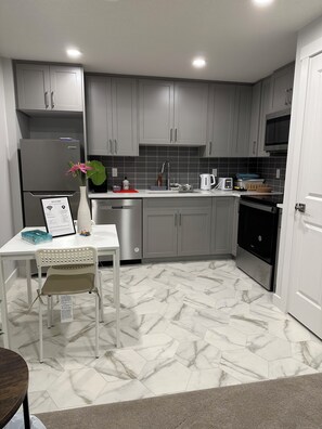 A modern kitchen with grey cabinets, a stainless steel refrigerator, a microwave, and a sink. - The Modern Nest (calgary)