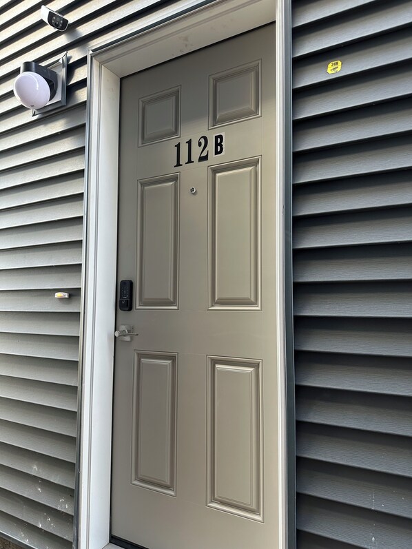 A beige door with the number 112B, a keypad lock, and a peephole. - The Modern Nest (calgary)