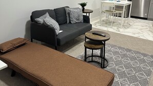 En kompakt opholdsstue med sofa, lille bord, bænk og et tekøkken.