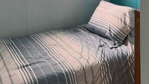 Een kleine kamer met een enkel bed, een raam, een muur in teal en een bed met een patroon.