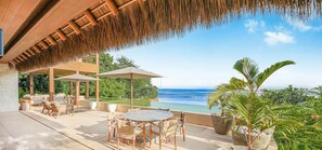 Relax on the ocean-view terrace surrounded by lush greenery and shaded by umbrellas.