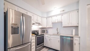 Una cocina moderna con electrodomésticos de acero inoxidable, armarios blancos y una mesa de comedor de vidrio.