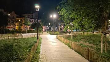 Un camino pavimentado bordeado por vallas de madera y faroles, que conduce a un edificio con ventanas iluminadas.