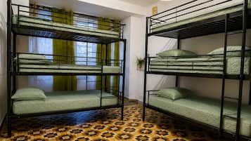 Tweepersoonsbed met groene beddengoed in een kamer met een patroon vloer en een raam met gordijnen.