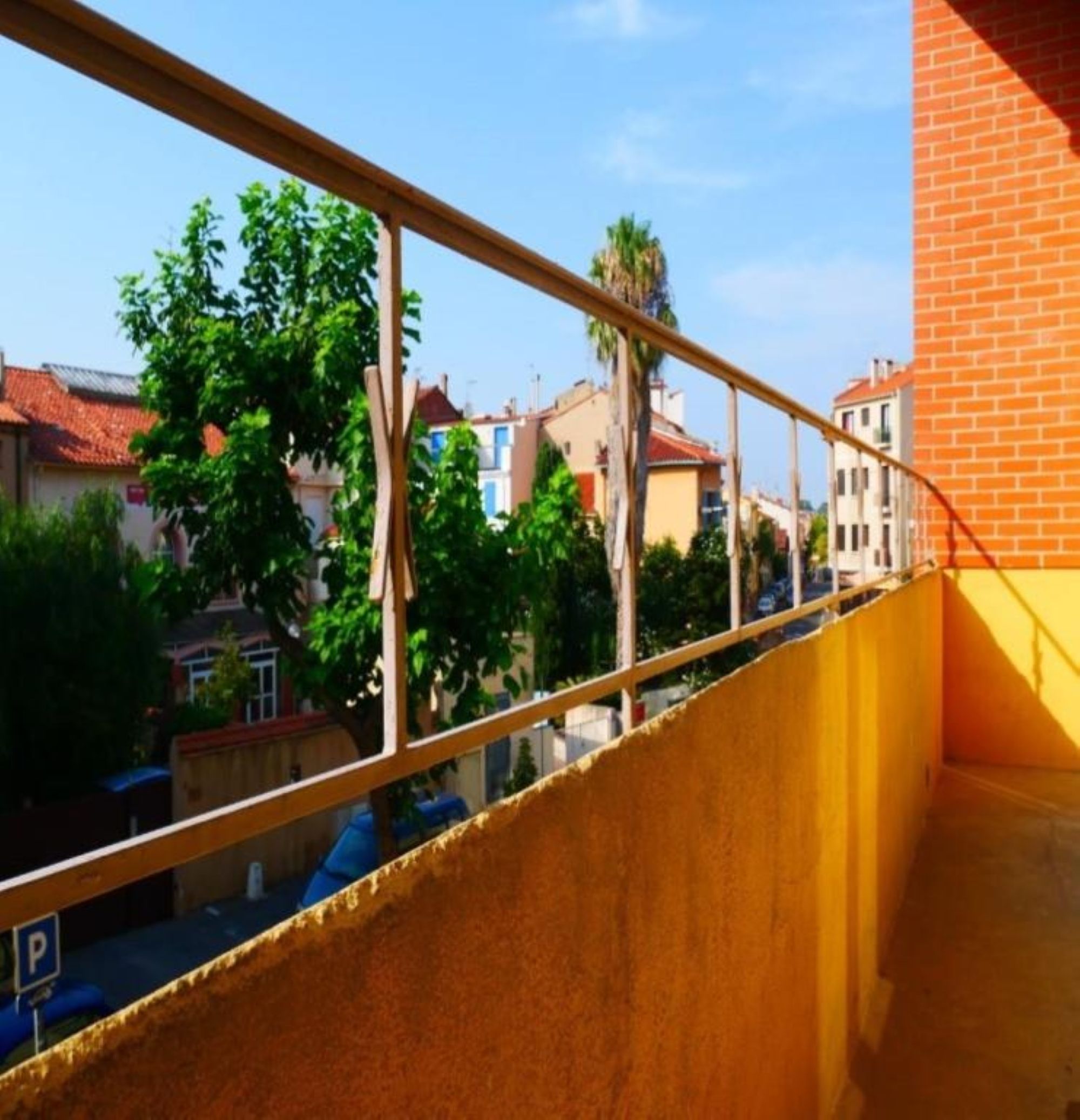 Un balcón con barandilla de metal que da a una calle con edificios y árboles.