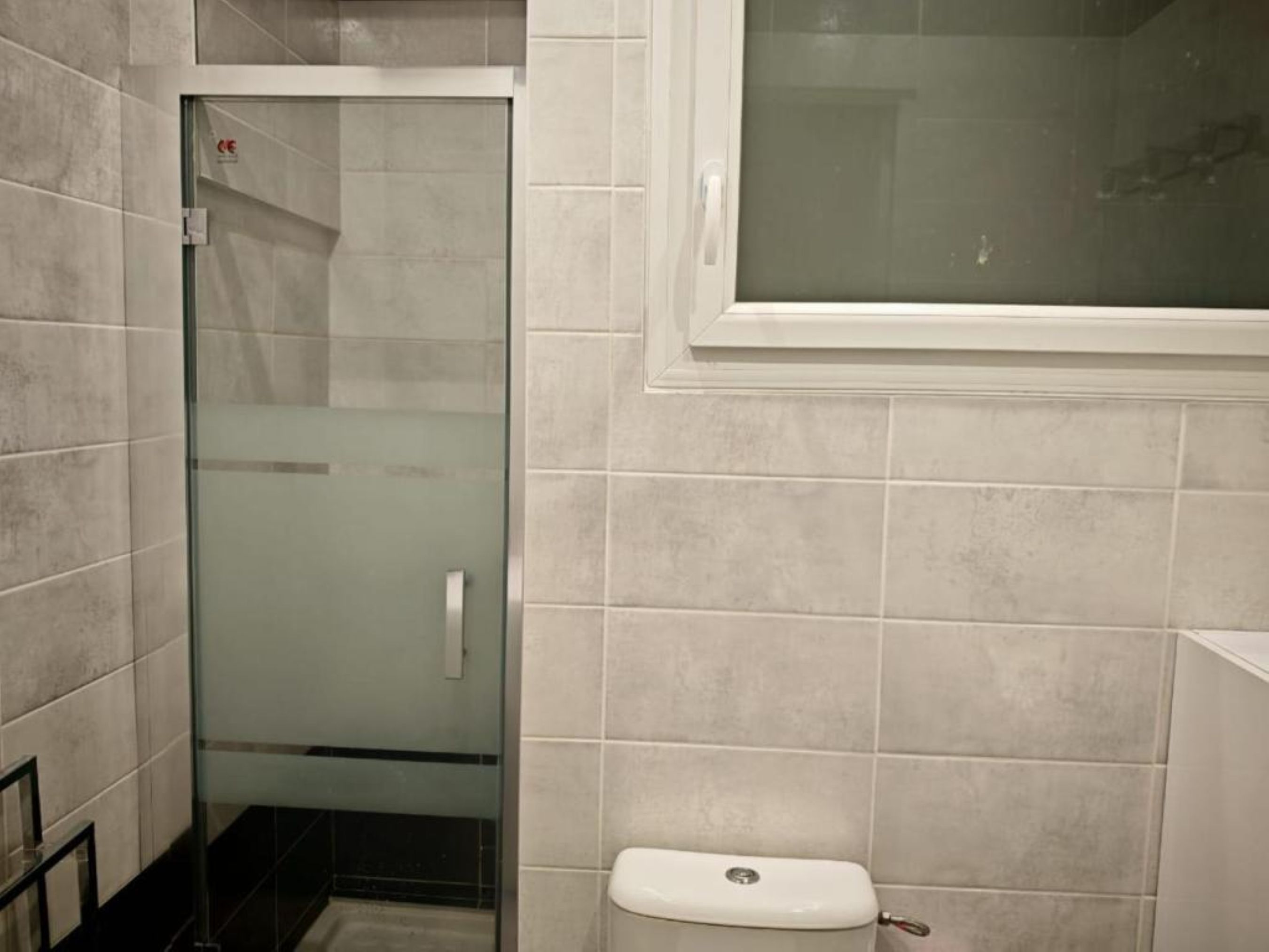 Un baño con ducha envuelta en vidrio, inodoro y pared de azulejos.