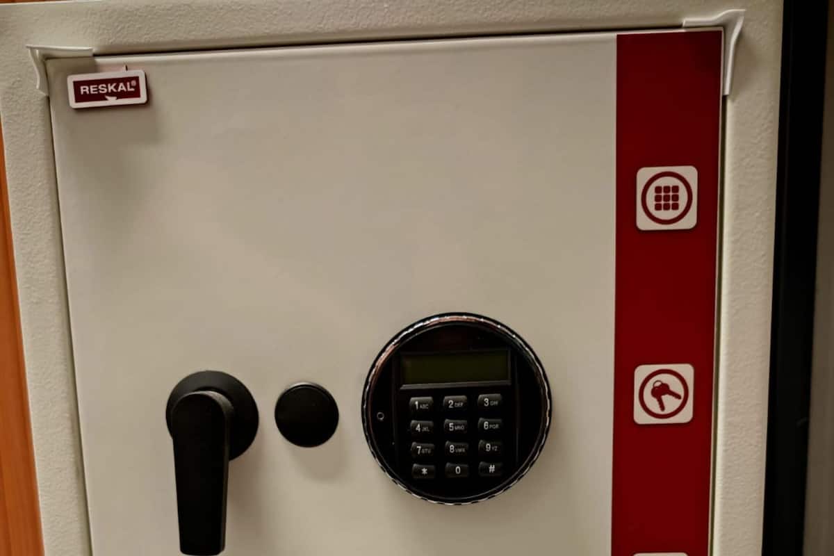 A safe with a digital keypad and a black handle, featuring multiple security symbols on its side.