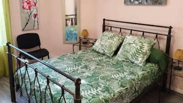 Un dormitorio con cama, una silla, aire acondicionado, un cuadro y un espejo.