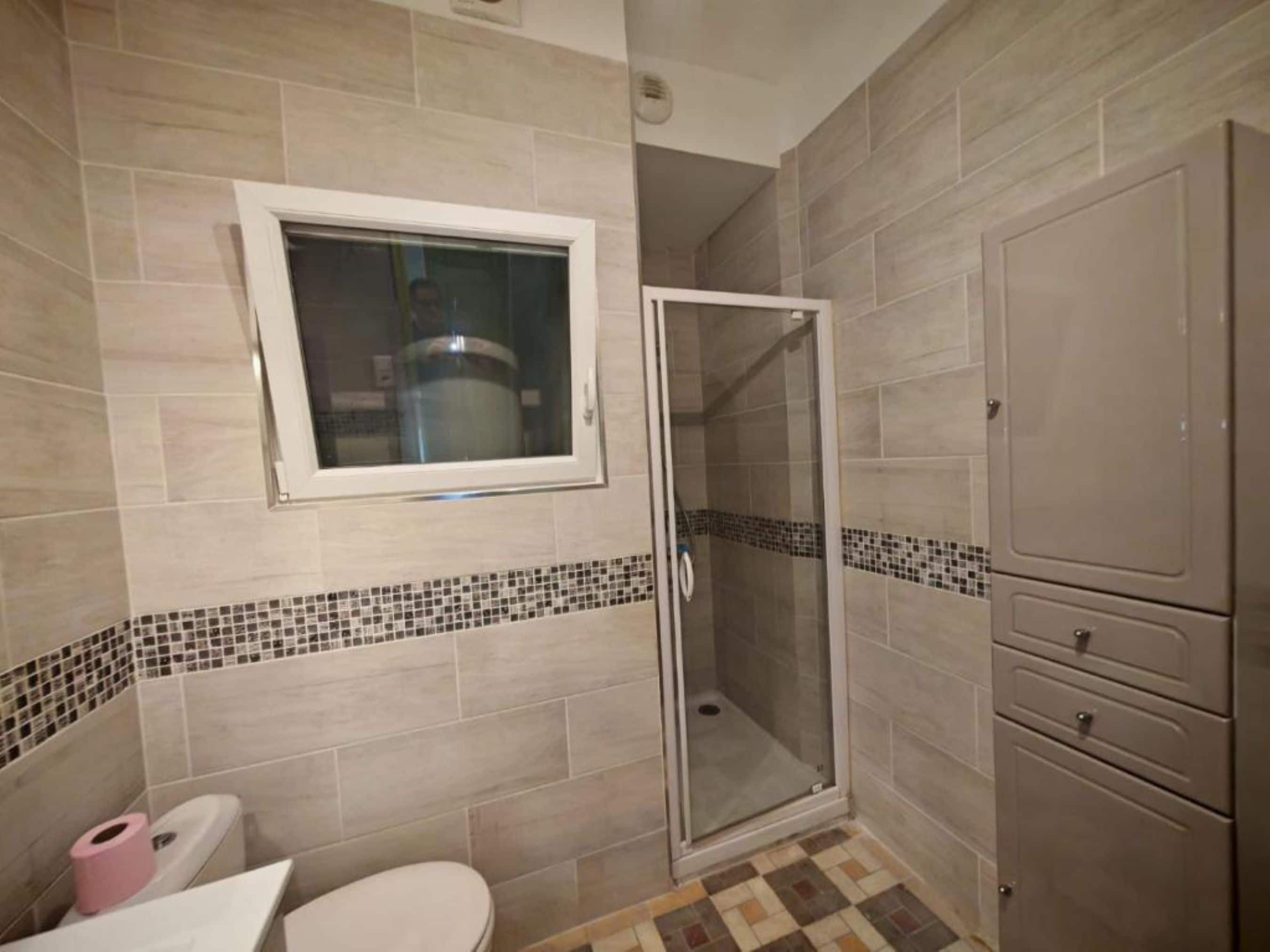 Un baño con inodoro, ducha con puerta de cristal y un armario.