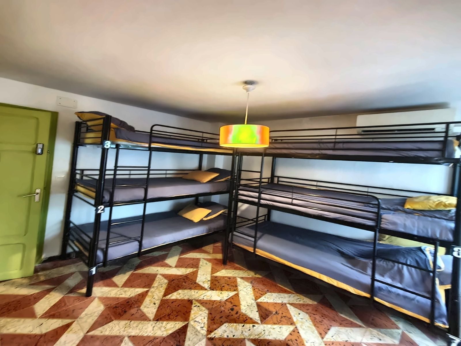 Habitación con literas, piso con estampado geométrico, puerta verde y una lámpara colgante.