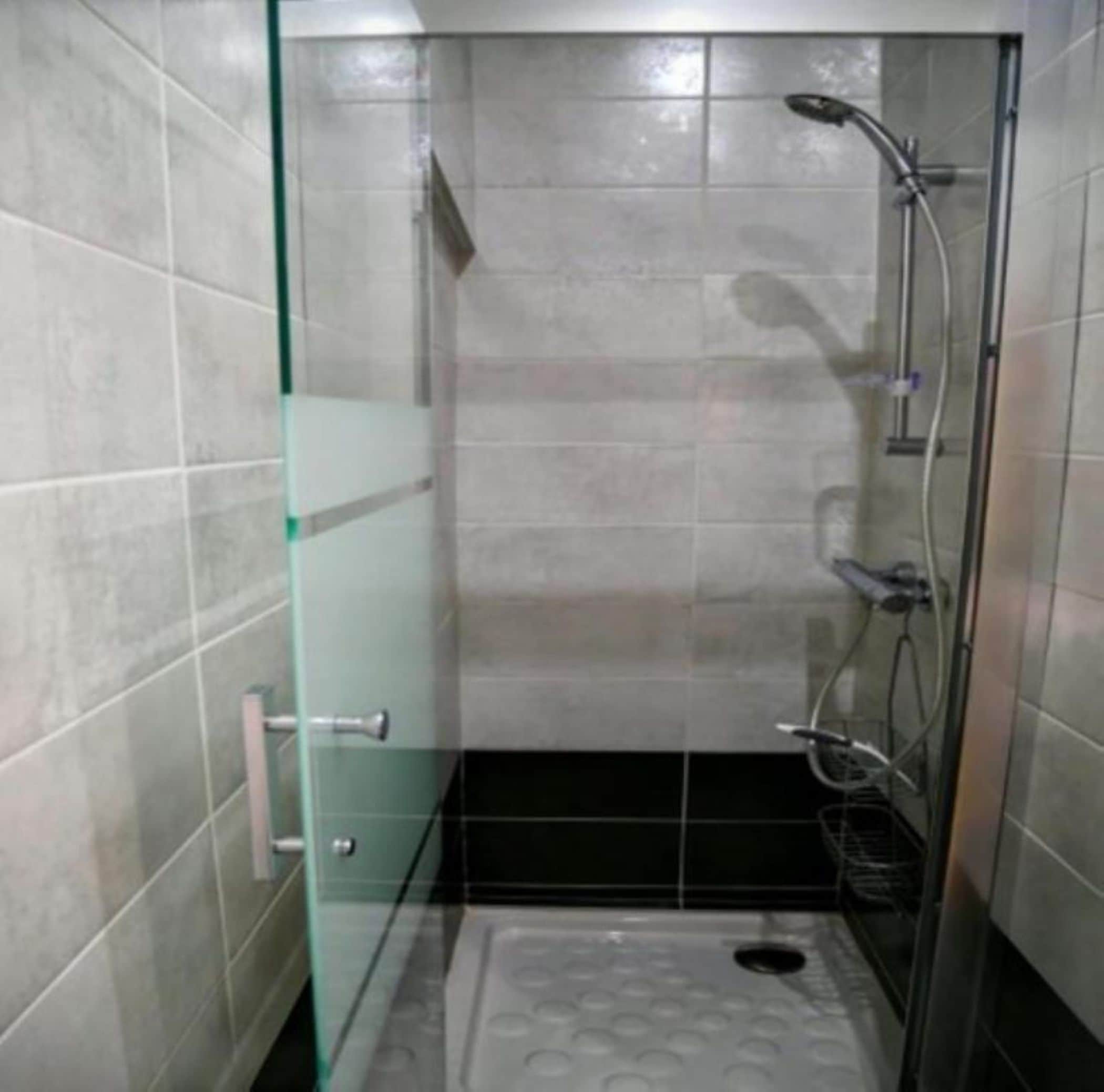 Un área de ducha pequeña y cerrada, con paredes de azulejos y puerta de cristal.