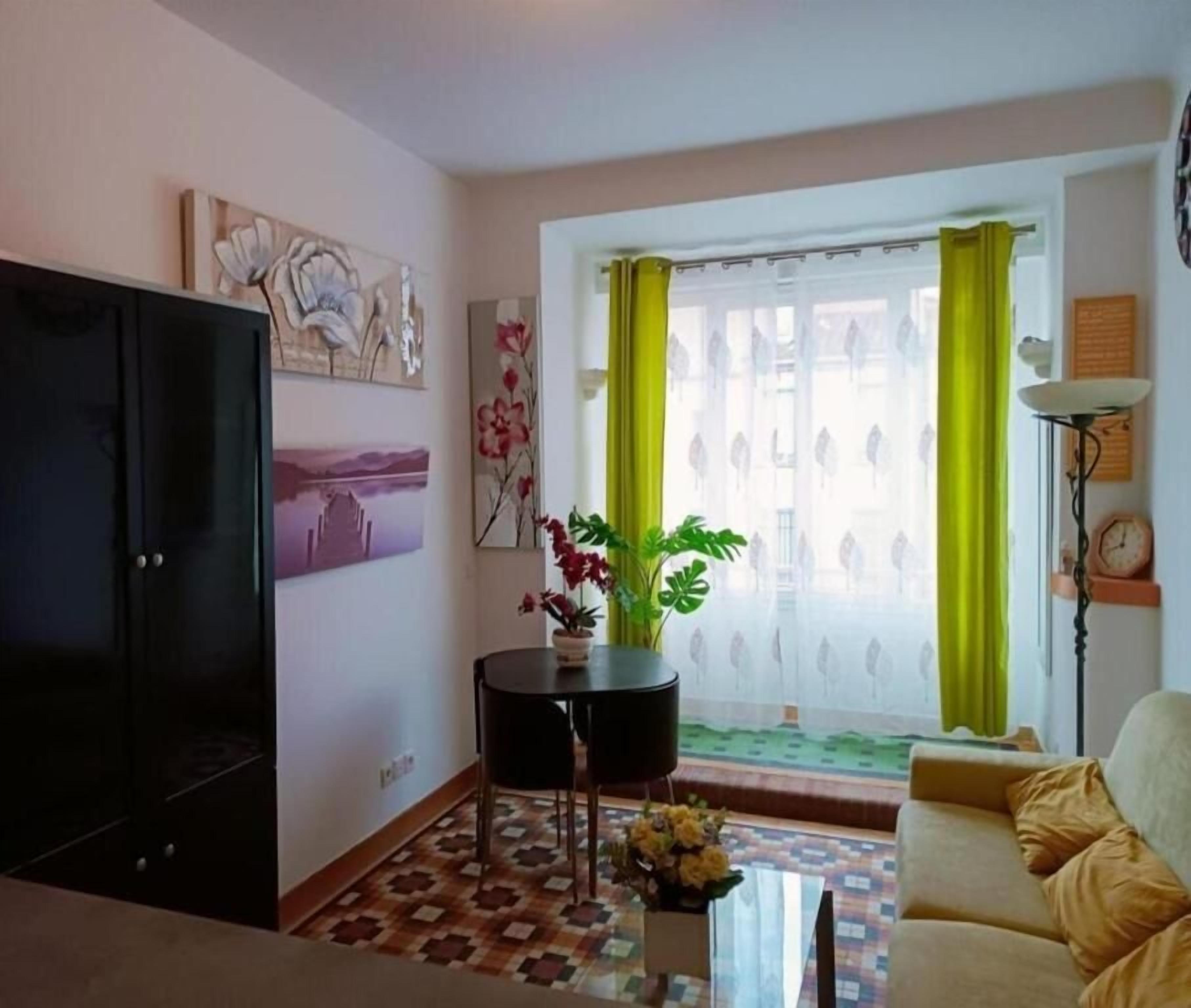 Una sala de estar con sofá, televisión, planta y ventana con cortinas.
