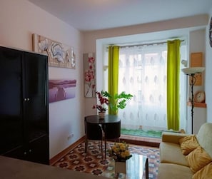Un salon avec un canapé, un téléviseur, une plante et une fenêtre avec des rideaux.