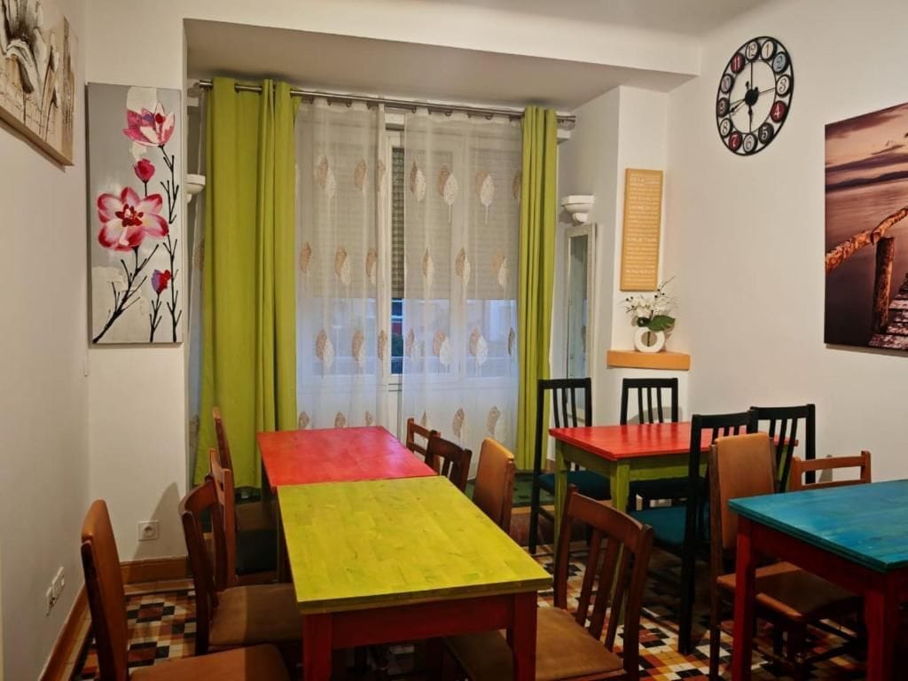 Un comedor con una mesa y sillas, una ventana con cortinas y adornos en la pared, incluyendo un reloj y un cuadro enmarcado.