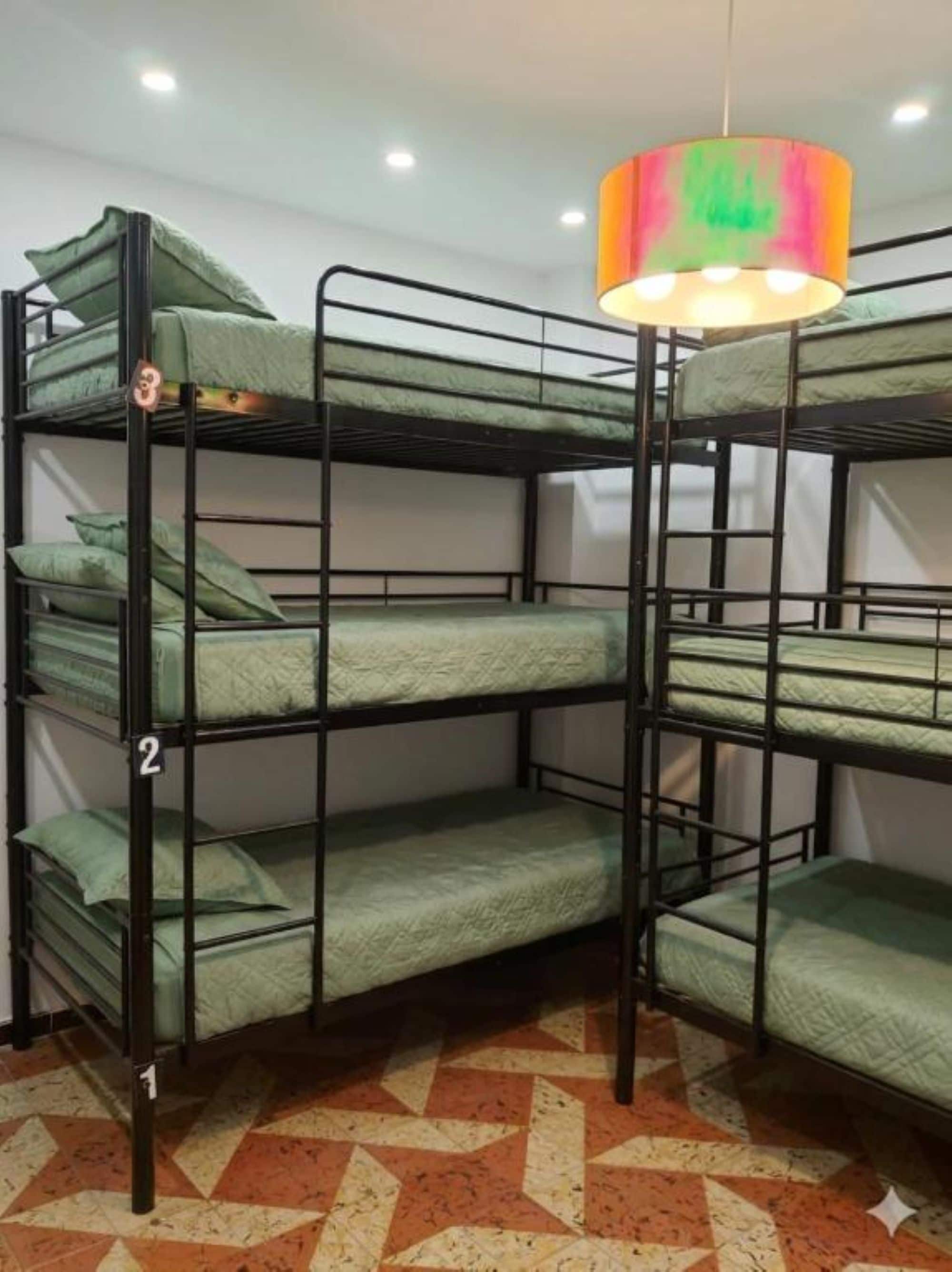Habitación con literas, suelo estampado, lámpara colgante y señal con un número a la izquierda.