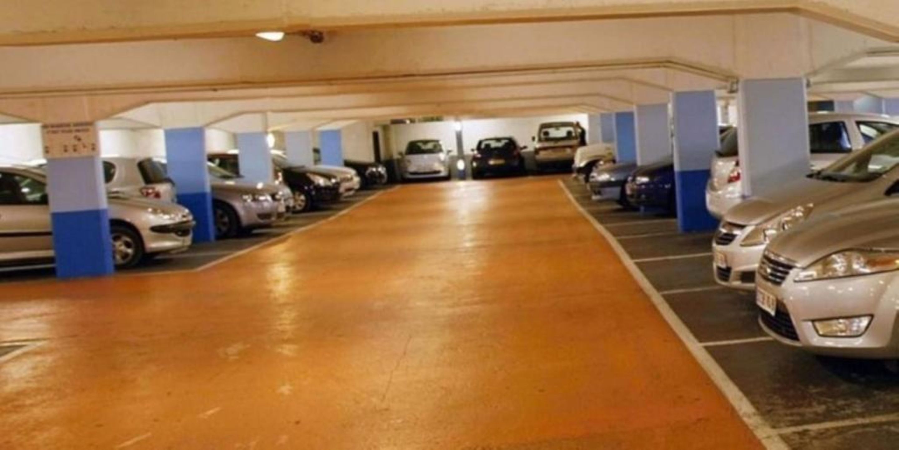 Un estacionamiento subterráneo de varios niveles con coches aparcados en filas.