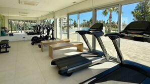 Een fitnessruimte met loopbanden, hometrainers en een bankje.