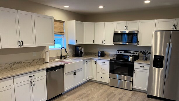 A modern kitchen with white cabinets, stainless steel appliances, and a wooden floor.