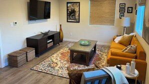 A modern living room with a flat-screen TV, dark wood furniture, a colorful rug, and a sofa with cushions.